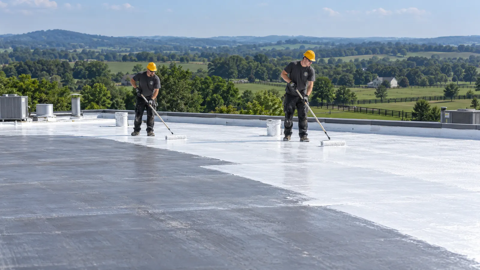 Crew applying white acrylic coating to a sloped metal roof